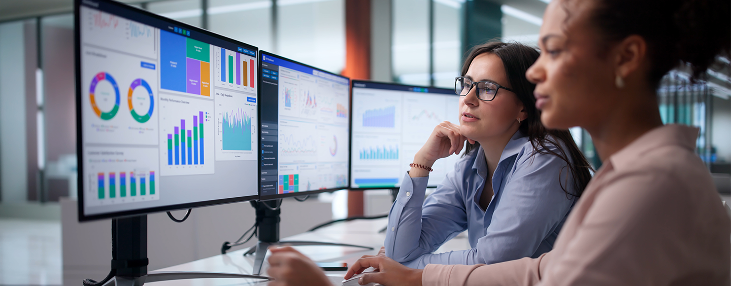 Two women sitting in an office looking at statistics on computer screens